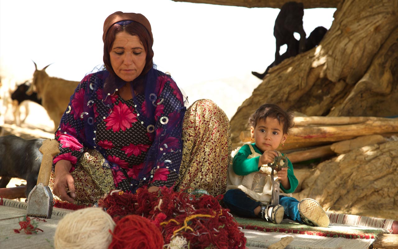 Nomad woman with child working on a rug